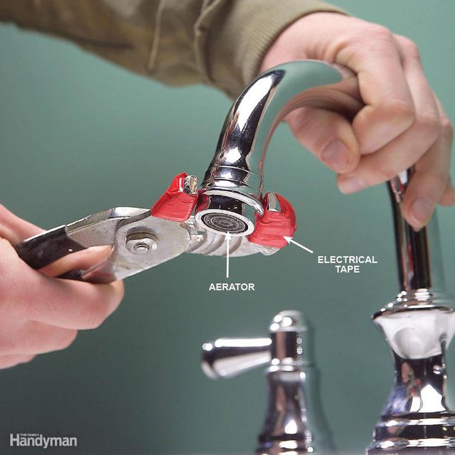 Une main utilise une pince pour dévisser le mousseur d'un robinet.