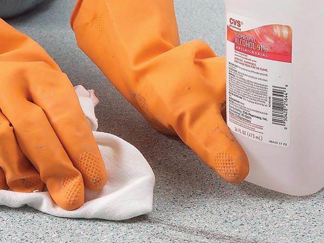 Des mains gantées nettoient une surface avec un chiffon et de l'alcool isopropylique.