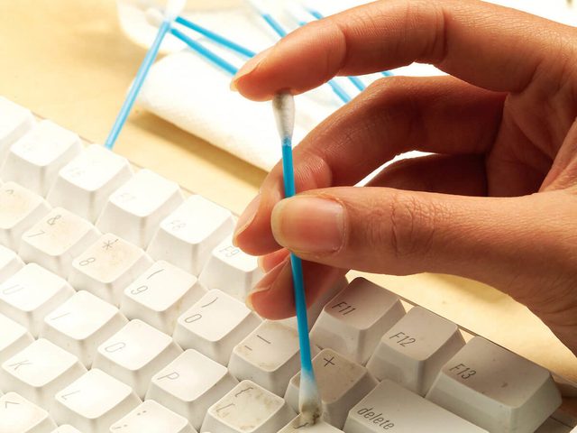Une main nettoie entre les touches d'un clavier avec un coton-tige.