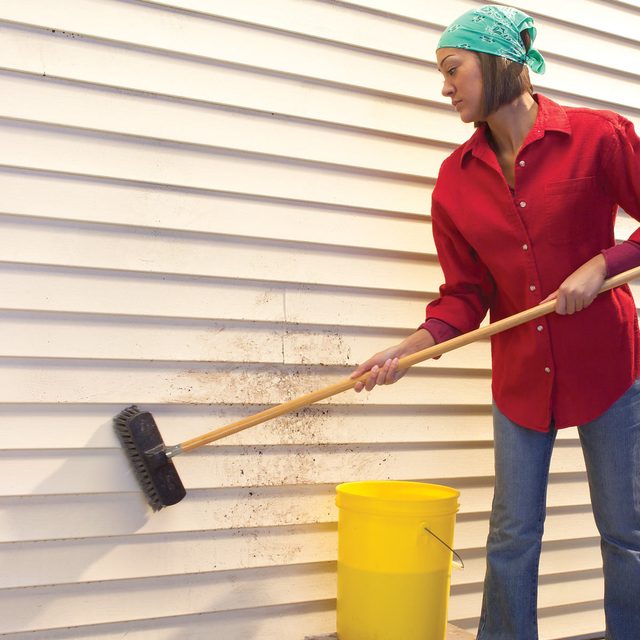 Une femme brosse le mur extérieur de sa maison.