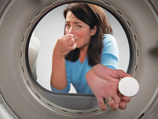 Une femme se pince le nez à côté d'un lave-linge malodorant.