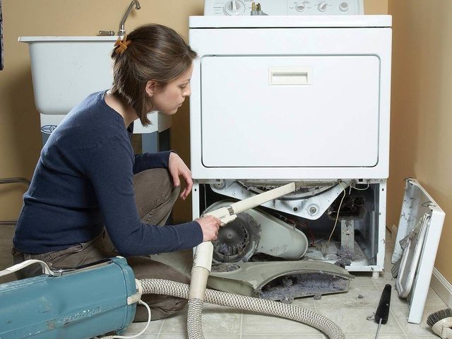 Une femme aspire la poussière à l'intérieur d'un sèche-linge démonté.