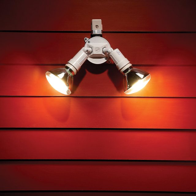 Un spot lumineux double éclaire un mur extérieur en bois rouge.