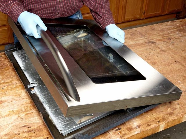 Une personne démonte la porte d'un four à micro-ondes pour la nettoyer.