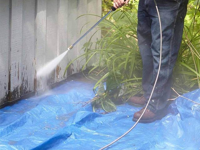 Une personne utilise un nettoyeur haute pression sur un mur extérieur.