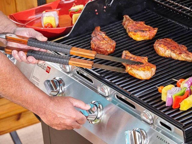 Une personne nettoie les grilles d'un barbecue à gaz.