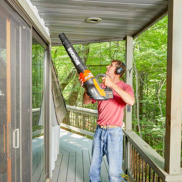 Un homme utilise un souffleur de feuilles pour nettoyer les aérations sous son toit.