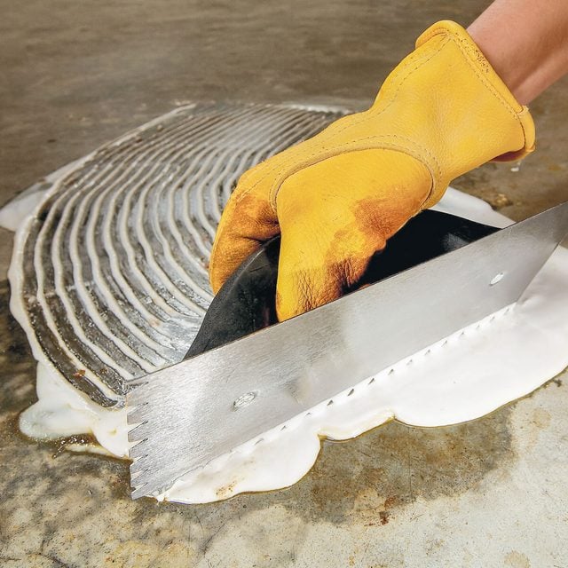 Une main gantée étale une pâte blanche sur une tache au sol avec une spatule.