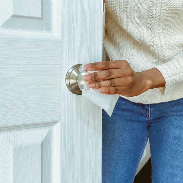 Une main nettoie une poignée de porte avec un chiffon.