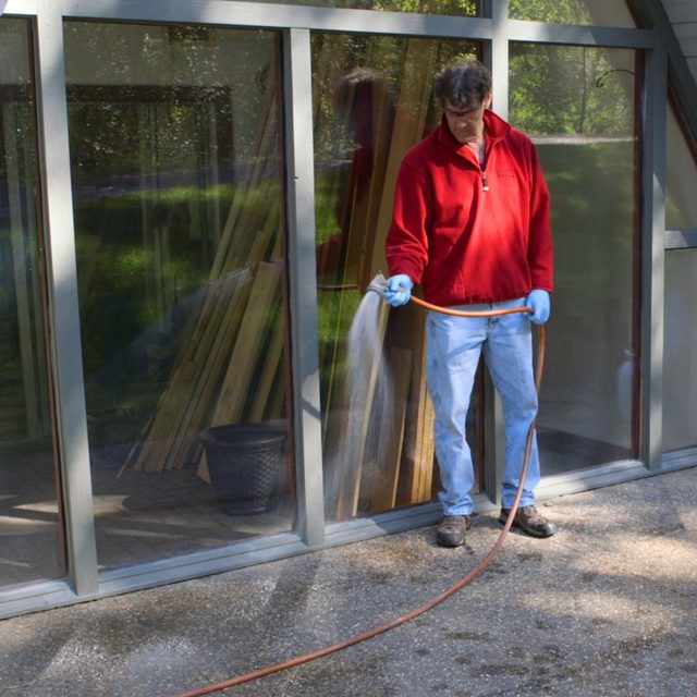 Un homme arrose une terrasse en béton avec un tuyau d'arrosage.