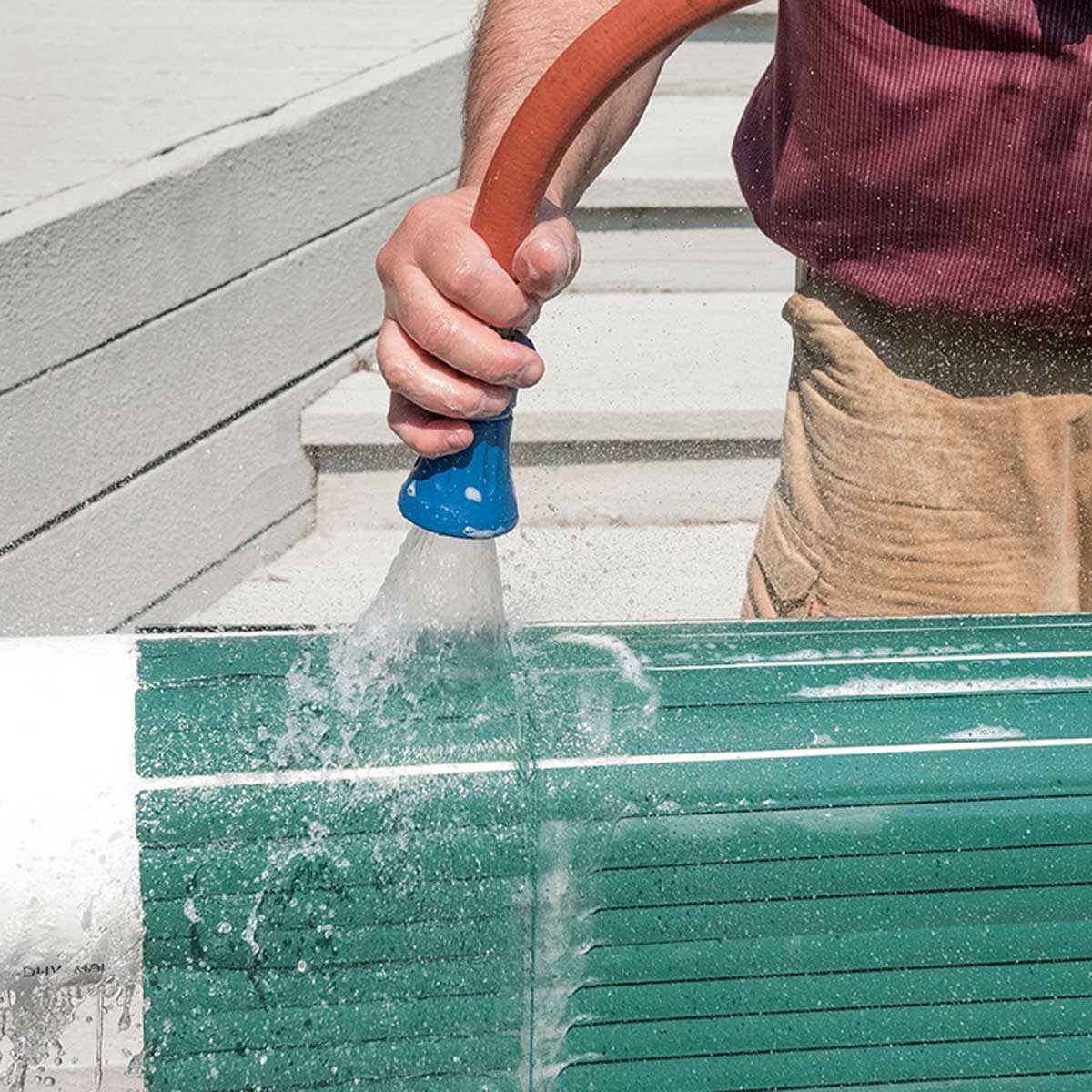 Un jet d'eau effectue le rinçage final d'un store vénitien vert.