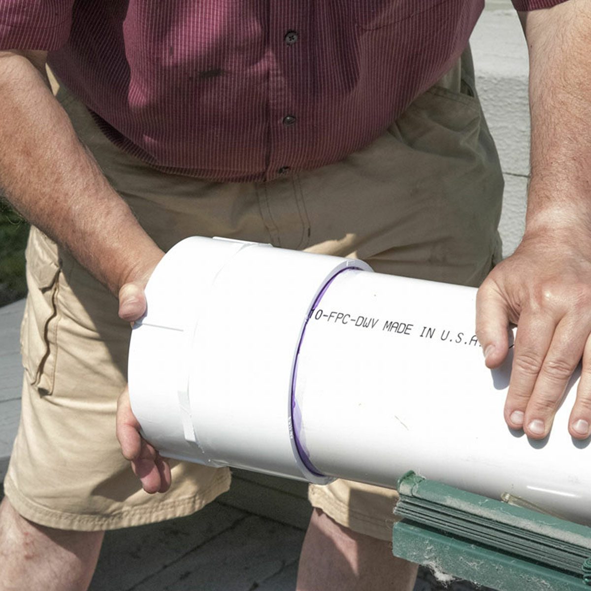 Une personne emboîte fermement un raccord sur un tube en PVC blanc.