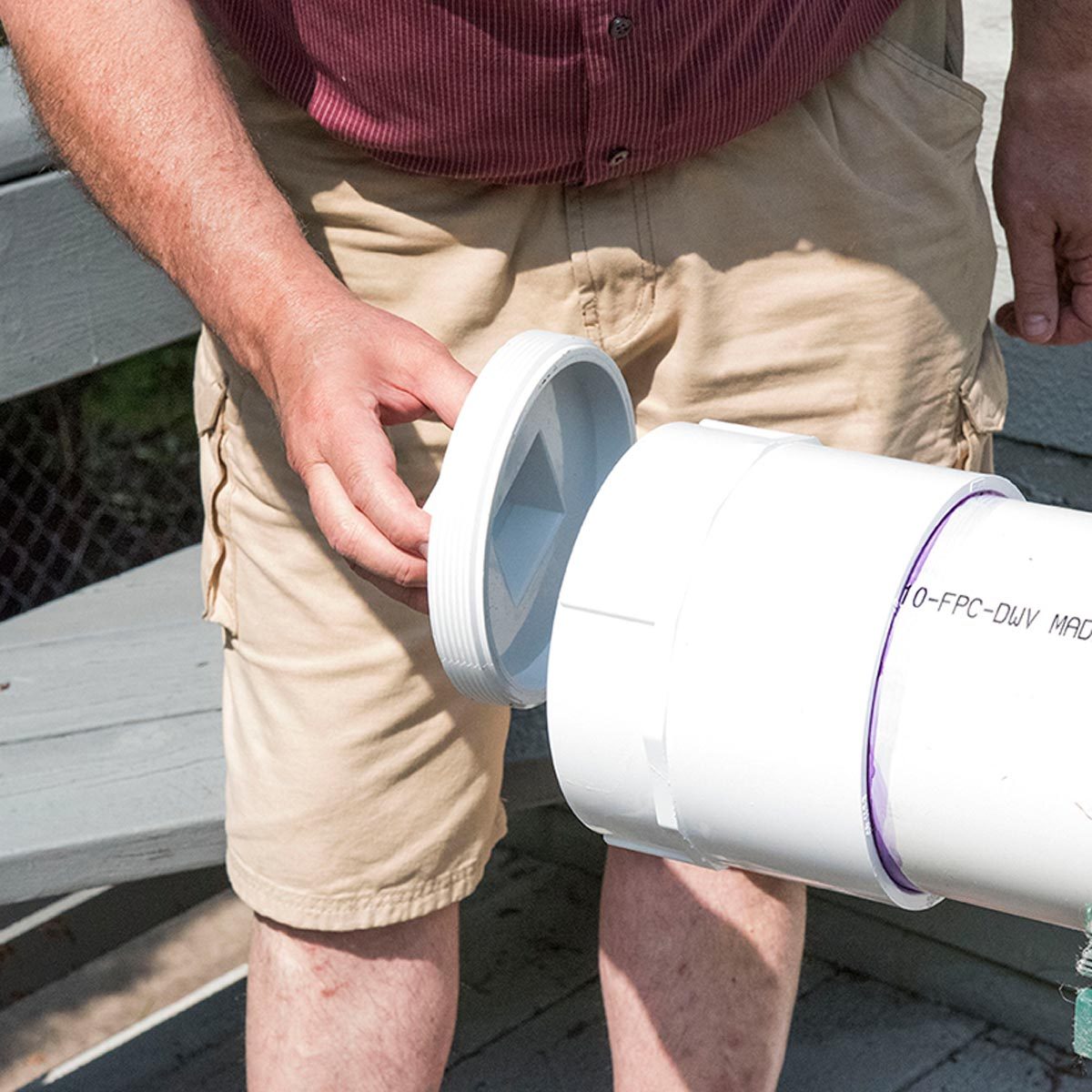 Une main s'apprête à visser un bouchon gris sur l'extrémité d'un tube en PVC.