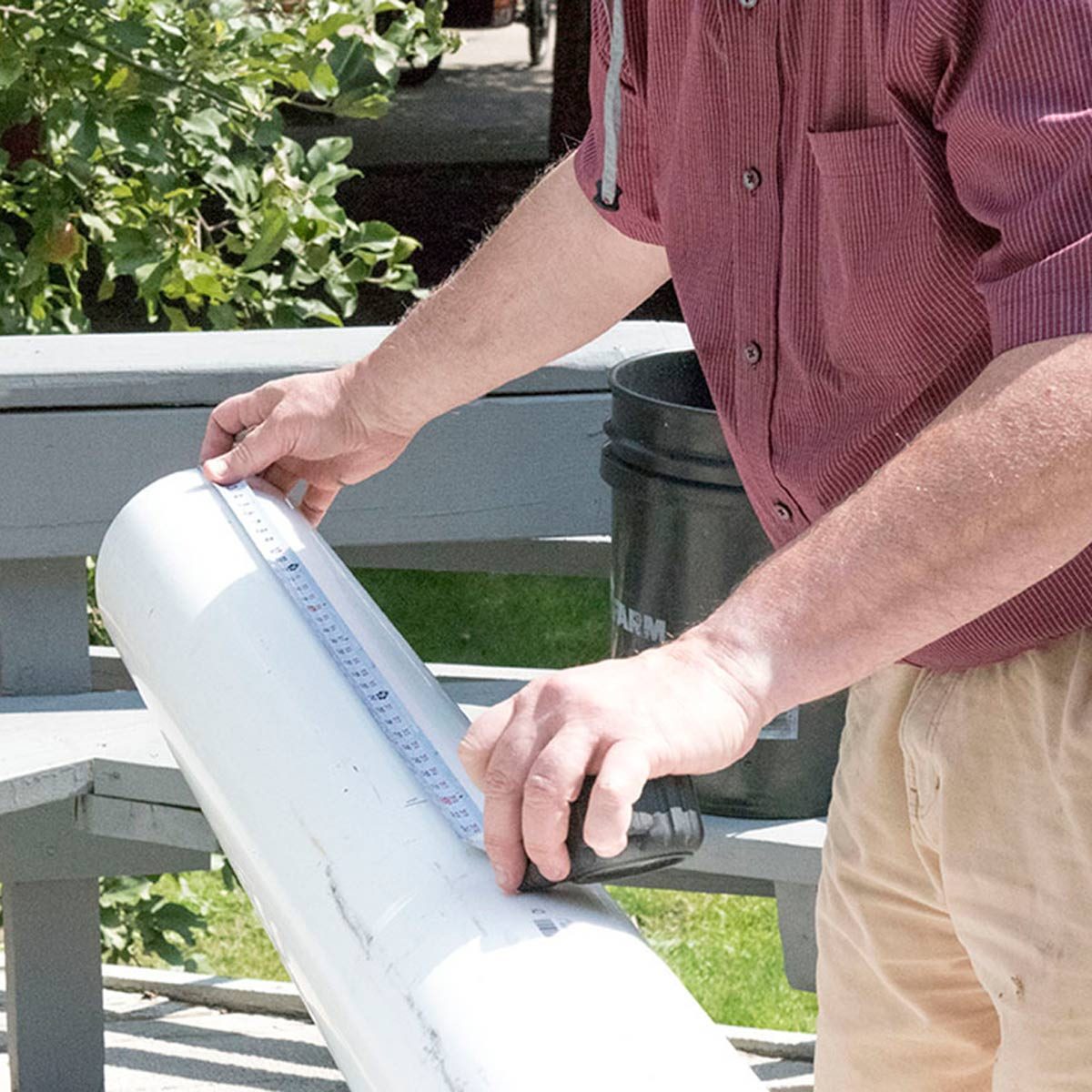 Un mètre ruban est utilisé pour mesurer la longueur d'un tube en PVC blanc.