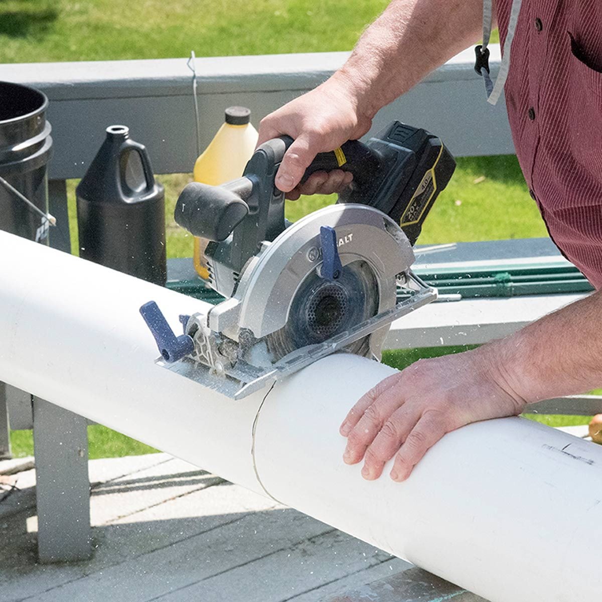 Une scie circulaire coupe un tube en PVC blanc posé sur une surface en bois.