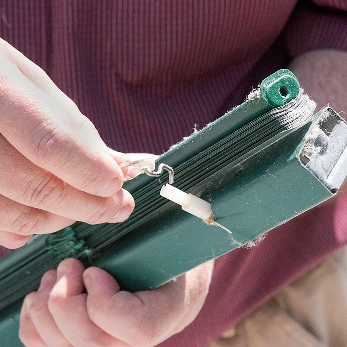 Une main retire le crochet métallique de la tige d'orientation d'un store.