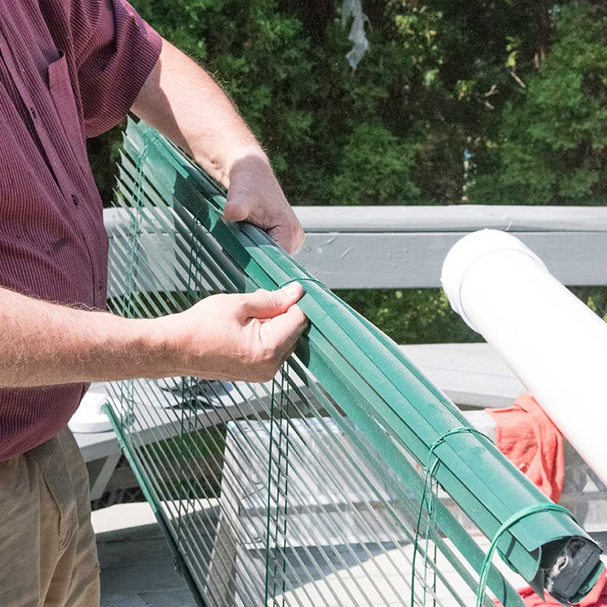 Une personne enroule un store vénitien vert sur lui-même.