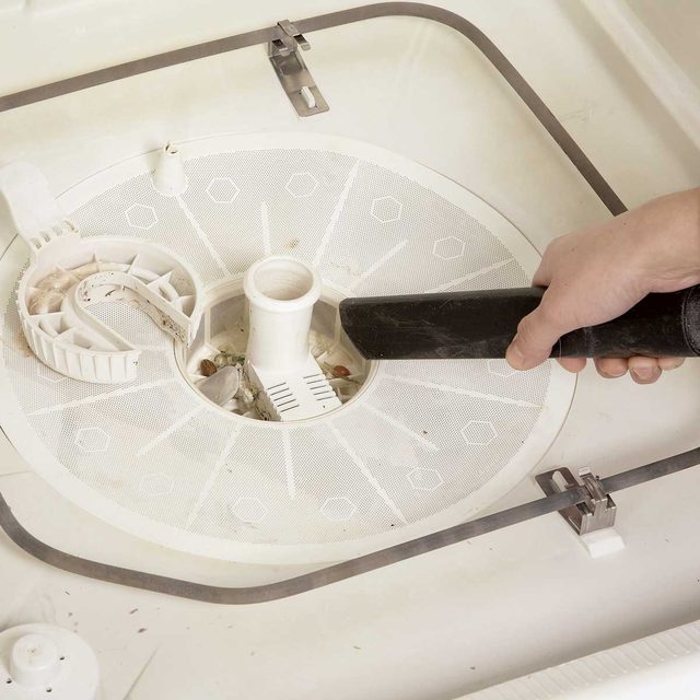 Une main utilise un aspirateur pour nettoyer le filtre au fond d'un lave-vaisselle.