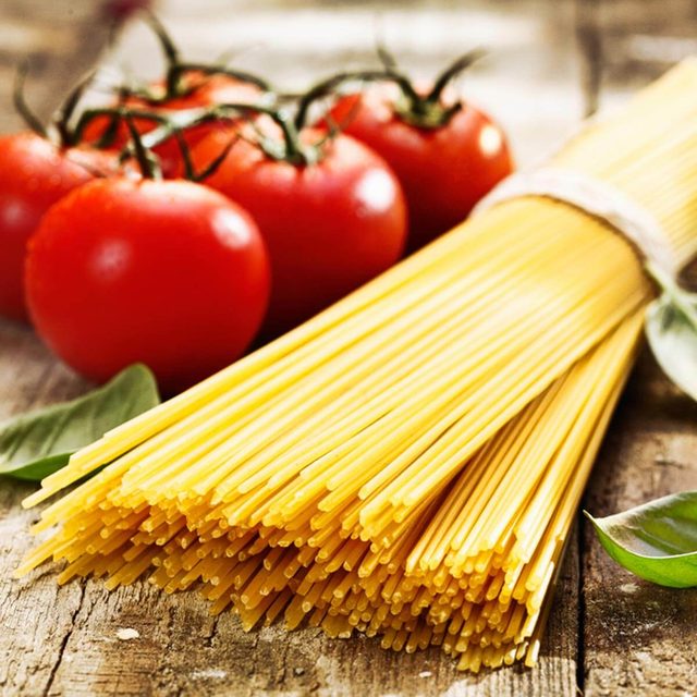 Spaghetti crus à côté de tomates et de basilic.