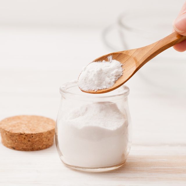 Une cuillère en bois remplie de bicarbonate de soude au-dessus d'un bocal en verre.