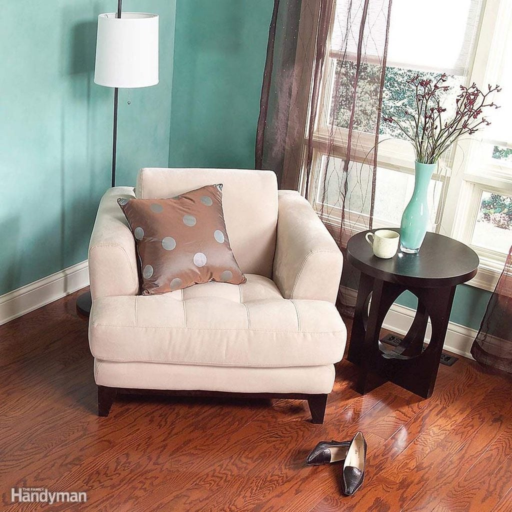 Un fauteuil beige avec un coussin à pois dans un salon aux murs bleu canard.