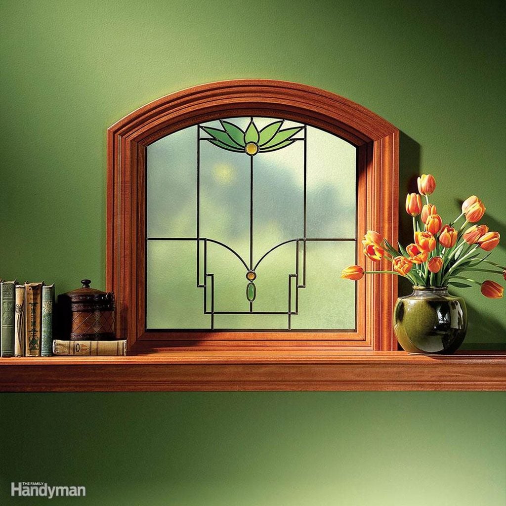 Une étagère en bois sous un vitrail, décorée de livres et d'un vase de tulipes.