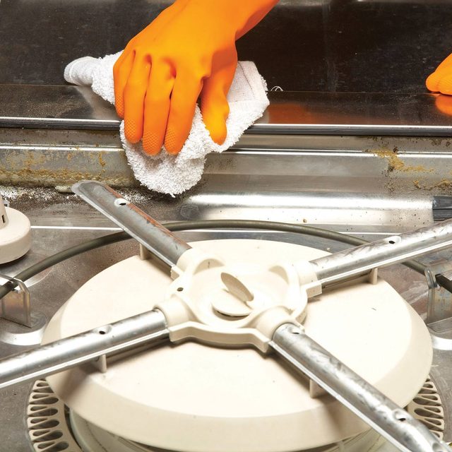 Une main gantée nettoie l'intérieur d'un lave-vaisselle