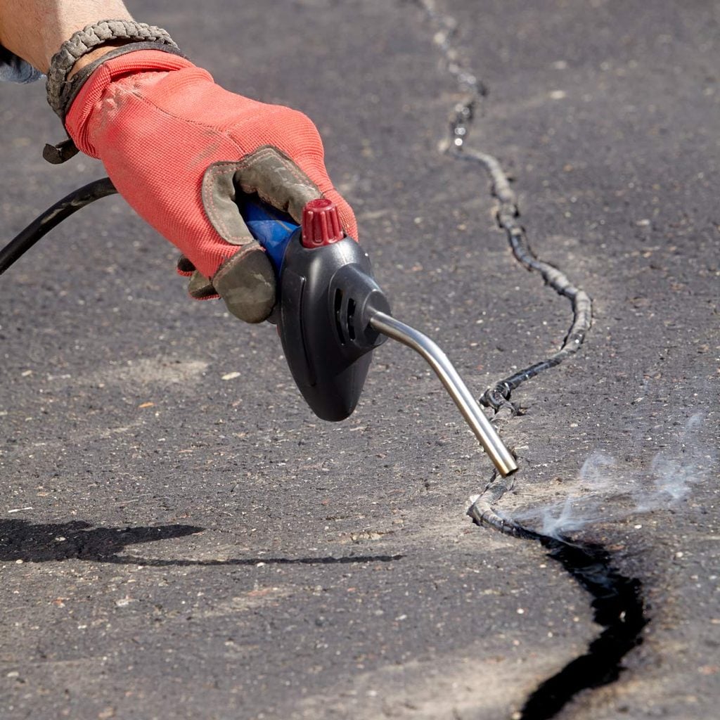 Une main gantée utilise un chalumeau pour réparer une fissure dans l'asphalte.