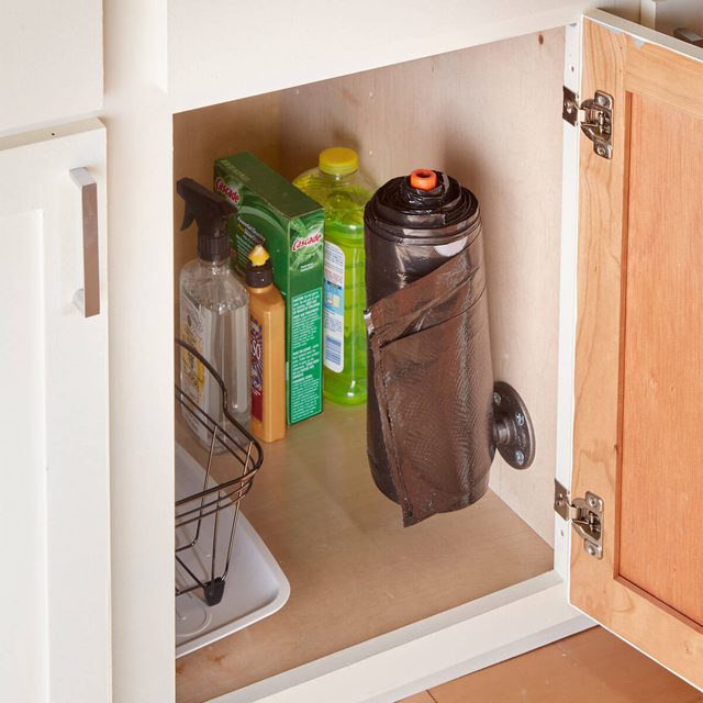 Un placard de cuisine avec des produits de nettoyage et un rouleau de sacs-poubelle fixé au mur.