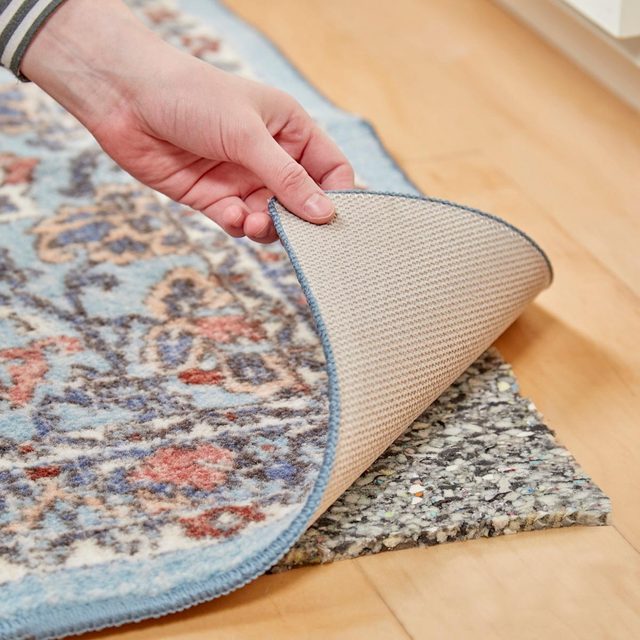 Une main soulevant le coin d'un tapis pour montrer une sous-couche épaisse en dessous.