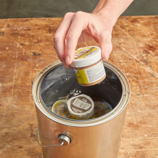 Une main tenant un petit pot au-dessus d'un récipient métallique rempli d'eau.