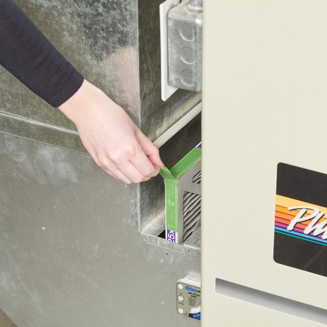 Une main tirant sur une languette en ruban adhésif pour retirer un filtre de chaudière.