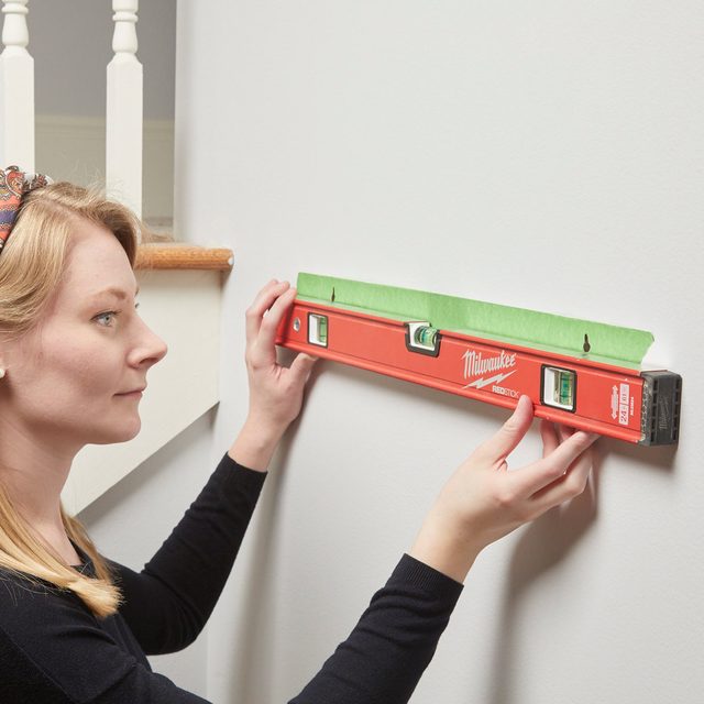 Une femme utilisant un niveau et du ruban de masquage pour accrocher une étagère.