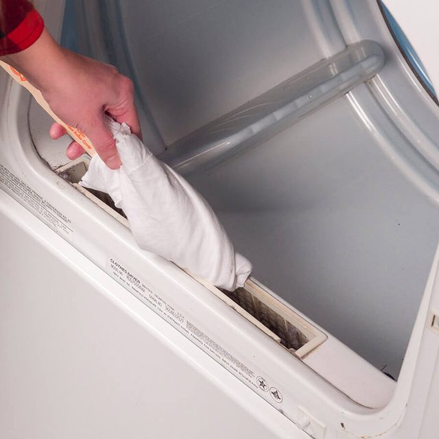 Une personne nettoie le logement du filtre à peluches d'un sèche-linge