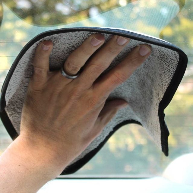 Une main essuie une vitre de voiture avec un chiffon.