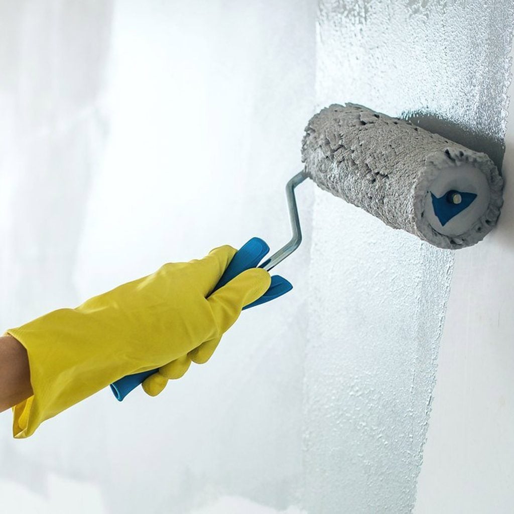 Une main gantée passe un rouleau de peinture sur un mur.
