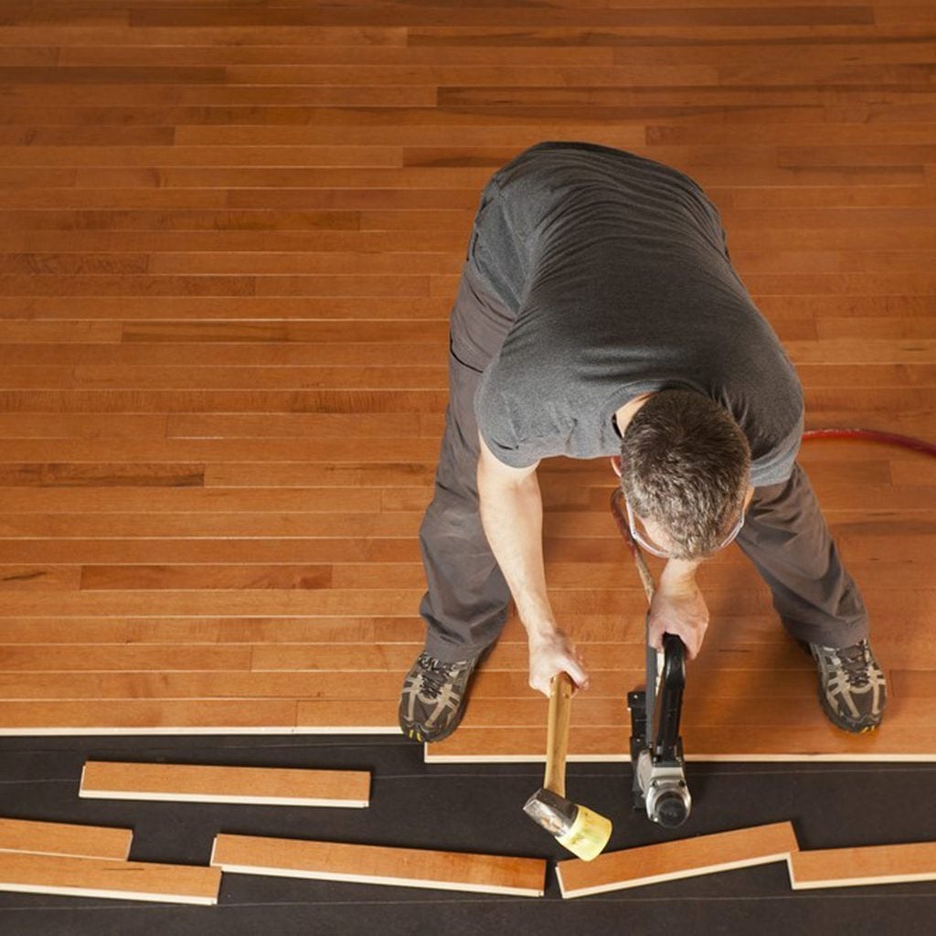 Un homme installe un parquet en bois à l'aide d'un marteau.