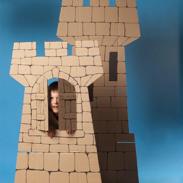 Un enfant regarde par la fenêtre d'un château en carton fait maison.