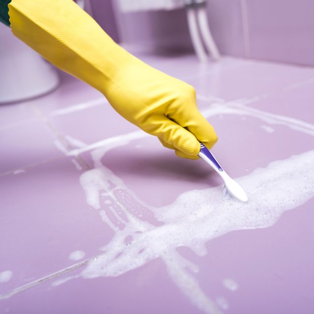 Une main gantée nettoie les joints de carrelage avec une brosse