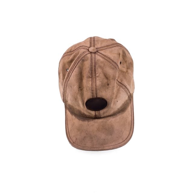 Une casquette marron usée posée sur une surface blanche.
