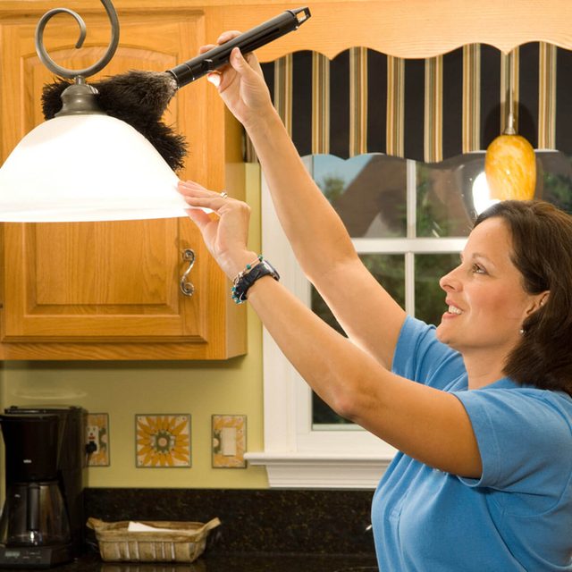 Une femme dépoussière un lustre de cuisine