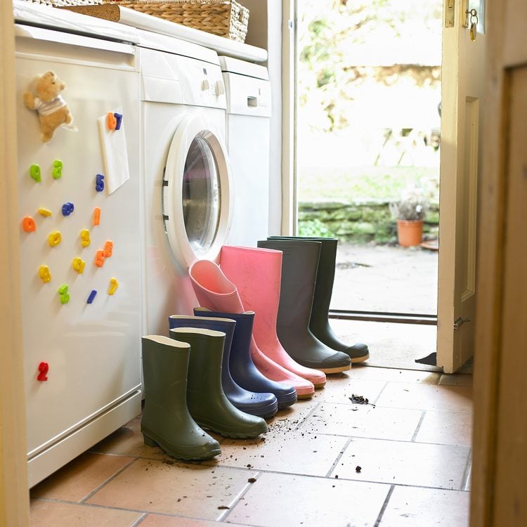 Bottes en caoutchouc colorées près d'une machine à laver, avec de la saleté autour.