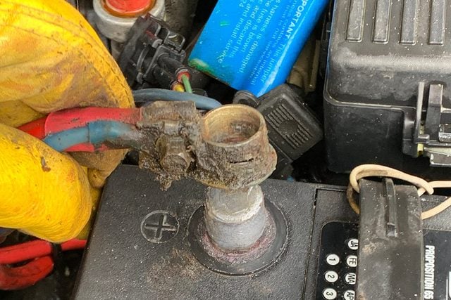 Une main serrant l'écrou d'une cosse de batterie avec une clé.