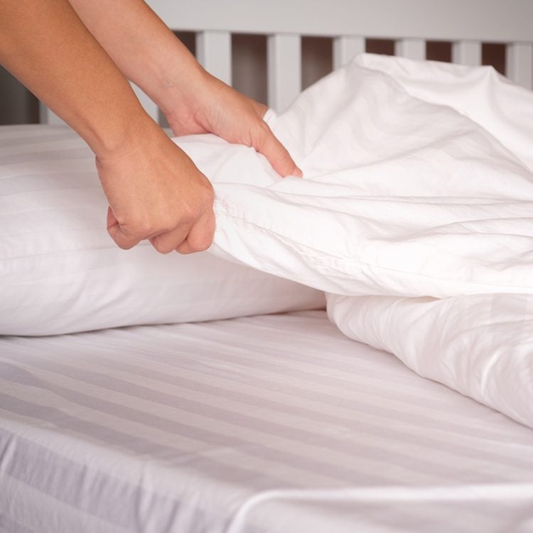 Une main qui ajuste une couette blanche sur un lit.