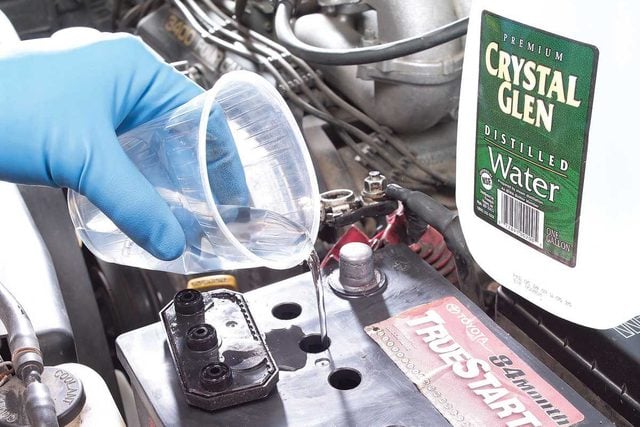 Une personne faisant l'appoint d'eau déminéralisée dans une batterie de voiture.