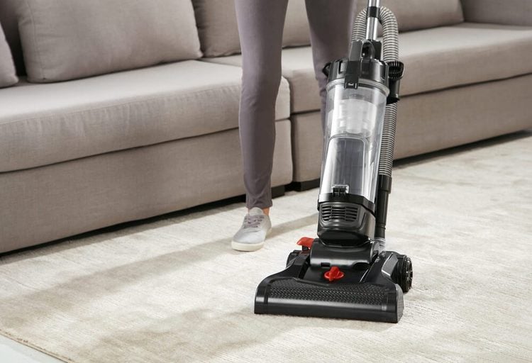 Une personne passant l'aspirateur sur un tapis beige.