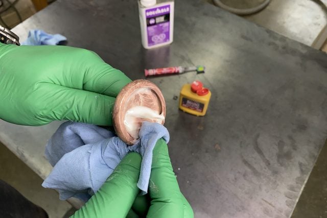 Une personne tient un petit objet rond et l'essuie avec un chiffon bleu, sur une table avec divers produits.