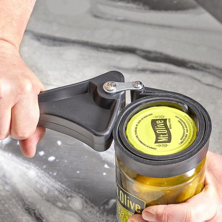 Une main utilise un ouvre-bocal à sangle pour ouvrir un bocal de cornichons.