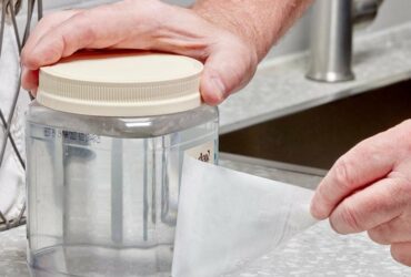 Une personne décolle une étiquette d'un bocal transparent dans une cuisine.