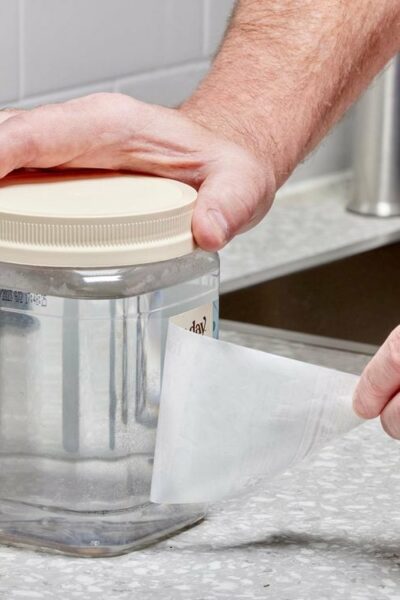 Une personne décolle une étiquette d'un bocal transparent dans une cuisine.